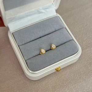 Close-up of teardrop gold earrings with round-cut clear zircon in a white jewelry box
