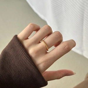 Detailed view of a golden twisted rope ring featuring minimalist braided texture on finger