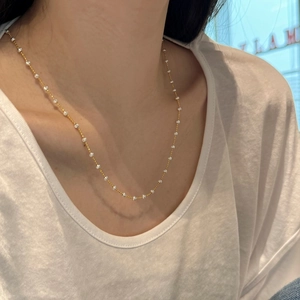 Detail of a gold S925 silver necklace with white beads on a female model
