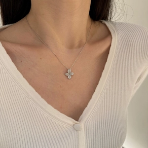 Close-up of a silver floral pendant necklace with full diamond pave on a model wearing white