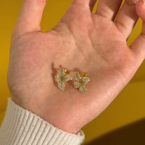 Macro view of gold-tone butterfly stud earrings with white zircon pavé setting on hand
