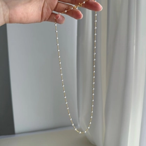 Detail of silver and gold beads on a delicate chain held against white fabric