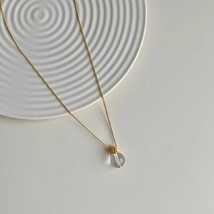 Detail of S925 silver gold necklace with round crystal pendant on a ceramic dish