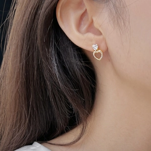 Close-up of heart-shaped gold earrings with sparkling zircons worn by a model