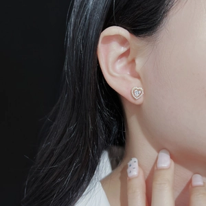 Close-up of heart-shaped gold stud earrings with sparkling crystals worn by a model