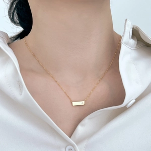 Dettaglio della collana minimalista a barra dorata con incisione a stella su modella