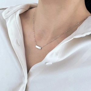 Dettaglio di una collana con pendente a barra in argento indossata su camicia bianca