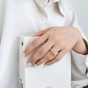 Detailed view of a gold tassel ring with dangling metal spheres on a model's hand