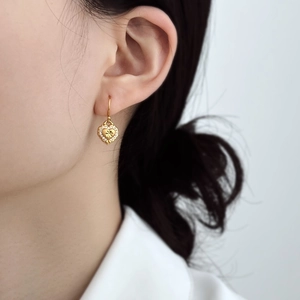 Detailed close-up of a gold heart drop earring with crystals and French hook on a model