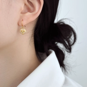 Detailed view of heart-shaped gold drop earrings with sparkling zirconia on a female model