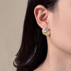 Close-up of fan-shaped gold stud earring with heart zircon worn on ear
