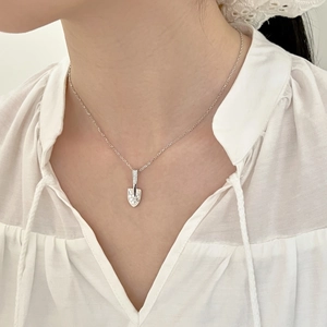 Macro detail of silver shovel pendant with pavé set crystals on a delicate chain