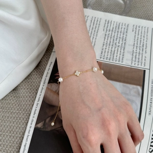 Detail eines goldenen Kleeblatt-Armbands mit Perlen und Kristallen auf seidigem Hintergrund