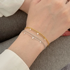 Détail de chaînes superposées dorées et argentées avec petits pendentifs en cristal au poignet