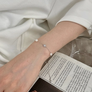 Detail der S925 Silberperlenkette mit glitzerndem Kleeblatt-Anhänger am Handgelenk