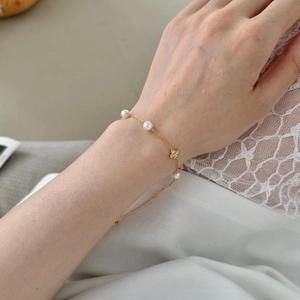 Detailaufnahme des vergoldeten Kleeblatt-Armbands mit eleganten weißen Perlen