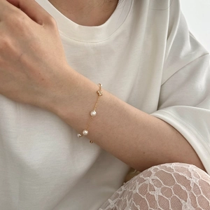 Detailansicht eines goldenen Perlenarmbands mit glitzerndem Kleeblatt-Anhänger am Handgelenk
