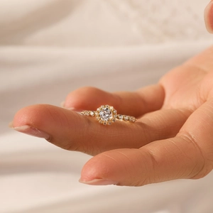 Detailed view of an 18K gold ring with a halo-set round diamond on a hand