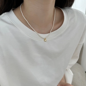Detailed close-up of a pearl necklace with a round golden zircon pendant on a model