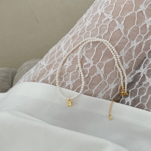 Detail of S925 pearl necklace with a gold zircon pendant on a soft lace background