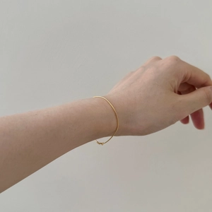 Close-up of a minimalist slim gold snake chain bracelet worn on a female wrist