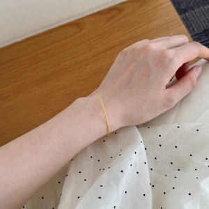 Detailed close-up of a slim golden bangle on wrist with textured metallic finish