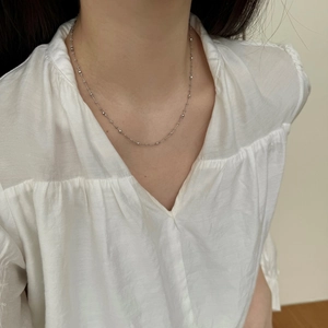 Délicat collier en argent fin S925 à billes porté par un mannequin avec un haut à col en V