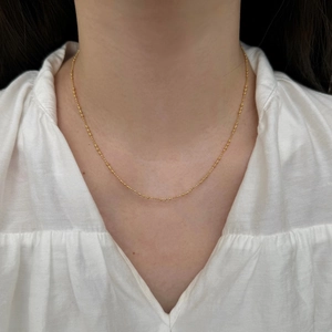 Gros plan d'un collier de perles dorées minimaliste porté sur un col de chemise blanc