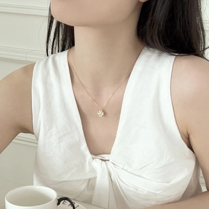 Macro shot of gold four-leaf clover pendant necklace worn by model on white linen