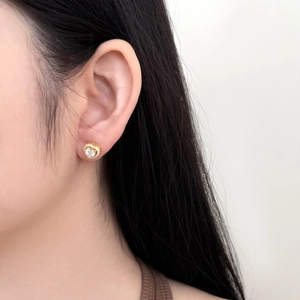 Close-up of heart-shaped gold stud earring with sparkling zircons worn on ear