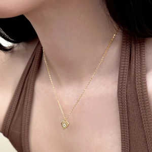 Gros plan du collier pendentif cœur doré avec pierre solitaire étincelante sur modèle