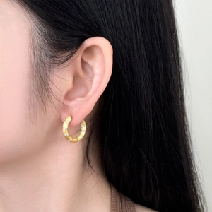 Macro detail of gold hoop earrings with matte finish and spiral zircon stones on model