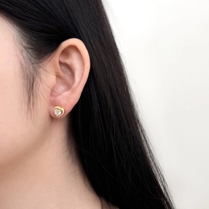 Close-up of heart-shaped gold studs with clear zircon worn on a female ear