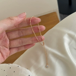 Detalle de pulsera de cuentas doradas con cierre de langosta y colgante de circonita clara