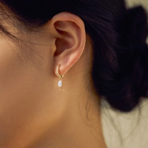 Close-up of elegant gold hoop earrings with sparkling zircon and oval gem pendant