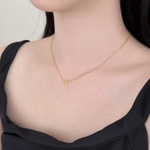 Close-up of a gold heart padlock pendant necklace on a delicate chain worn by a model