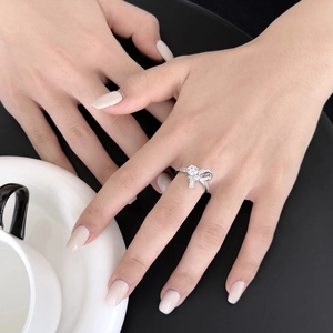 Close-up of S925 silver bow ring with zircon pavé setting on a hand with coffee