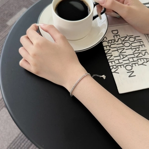 Close-up of a silver curb chain bracelet with a heart charm worn on a model's wrist