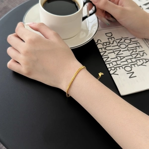 Close-up of gold curb chain bracelet with butterfly charm worn in a lifestyle setting