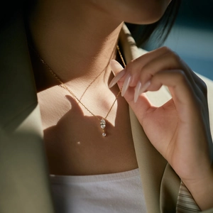 Close-up of golden marquise and round cut stone pendant on fine link chain worn by model