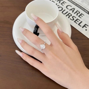 Primo piano di un anello in argento con diamante a pera su un dito in un set curato