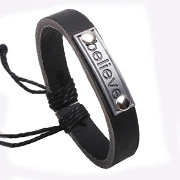 Dettaglio di un bracciale in pelle nera con placca in metallo incisa con la parola believe