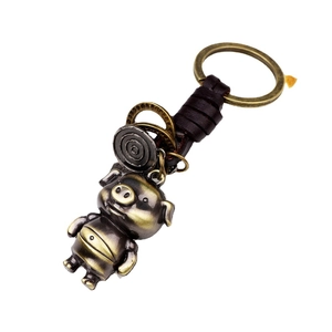 Porte-clés cochon vintage en bronze avec lanière en cuir et anneaux sur fond blanc