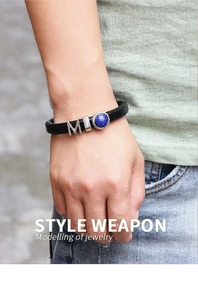 Détail du bracelet en cuir noir avec breloque lettre M et pierre turquoise bleue au poignet