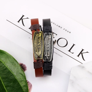 Vintage leather bracelet with antique metal feather charm on a minimalist background
