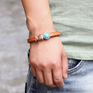 Bracelet en cuir marron avec lettres M en métal et pierre turquoise sur le poignet