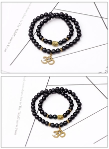 Détail de bracelets en perles noires mates avec tête de bouddha dorée et breloque symbole Om