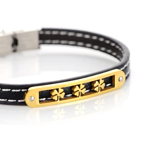 Close-up of black leather bracelet featuring three golden clover charms and white stitching