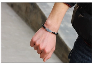Close-up of beaded bracelet with black matte beads and a zircon-set wing charm