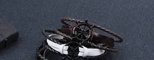 Detail of multi-layer leather bracelets featuring a black nautical ship wheel pendant